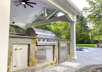 White pavilion over outdoor custom stone mosaic outdoor kitchen with pool in the front.